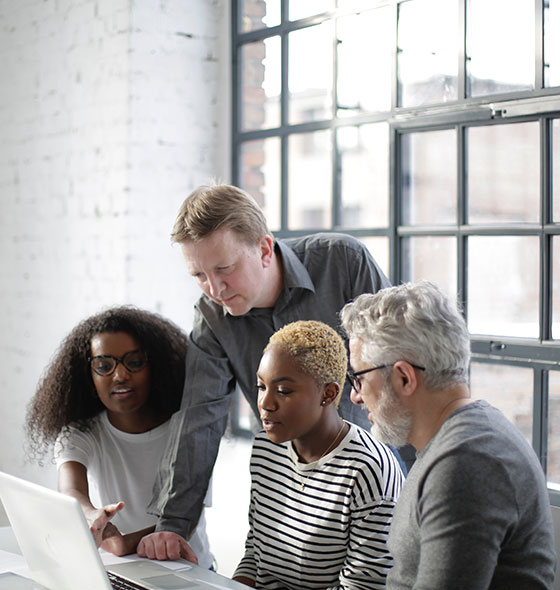 A group of people sitting around a laptop.