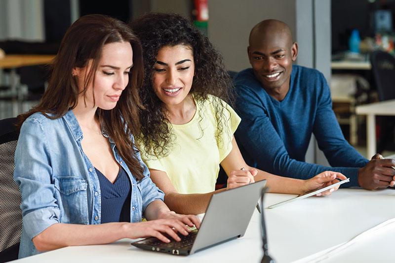 Three people sitting at a table looking at a laptop.